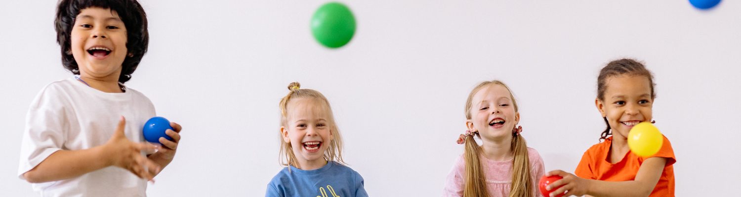 Four children of around 6 years old playing with colourful plastic balls and smiling.