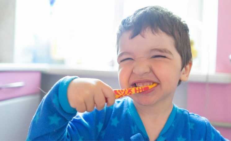 Close up of a young boy in blue pyjamas brushing his teeth.