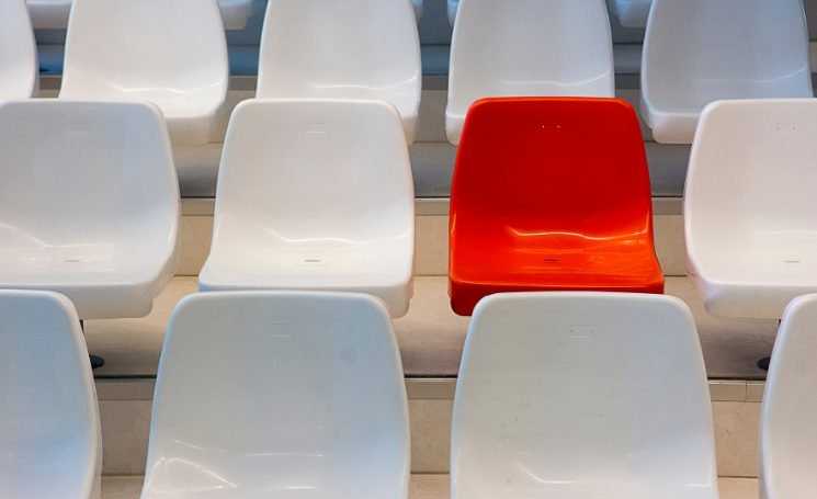 Several rows of fixed white plastic chairs, with one red chair among them