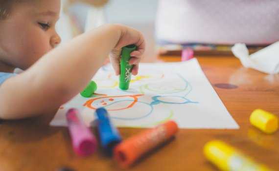 Young child draws with thick colourful crayons on a piece of paper