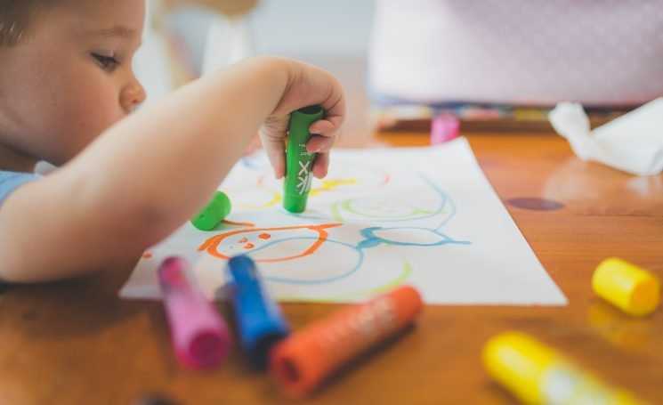 Young child draws with thick colourful crayons on a piece of paper